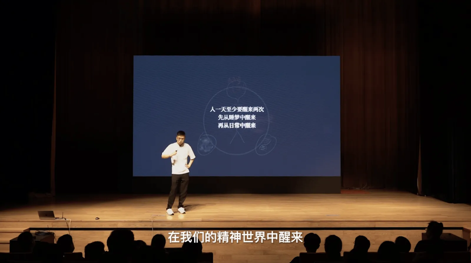 剧场舞台上,汤质站在大萤幕前,萤幕上写着:人一天至少要醒来两次,先从睡梦中醒来,再从日常中醒来