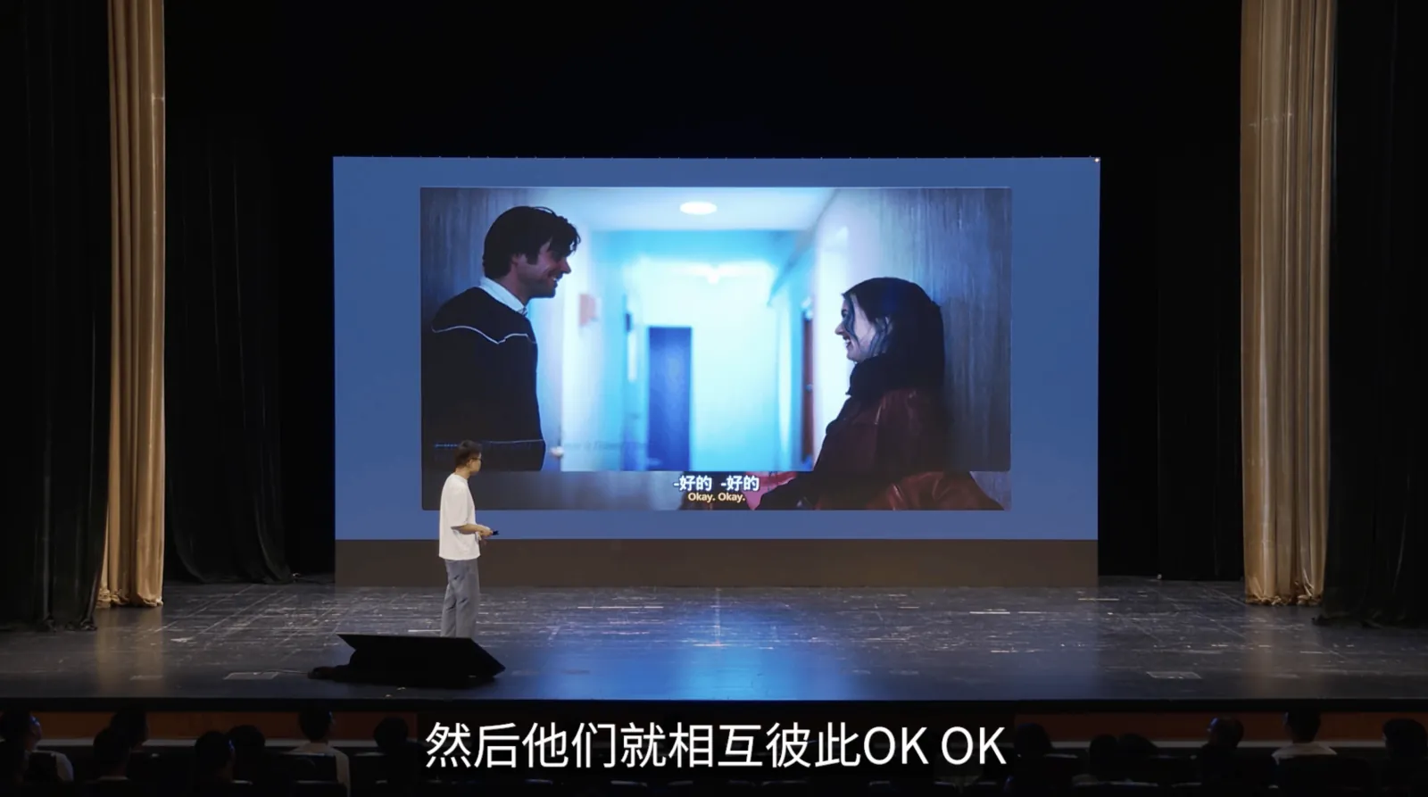剧场舞台上,汤质站在大萤幕旁,萤幕播放一段电影画面